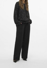 Zwarte trui met pailletten en lange, losse mouwen, gecombineerd met zwart, hoog getailleerd broek met een rechte snit en strakke lijnen.