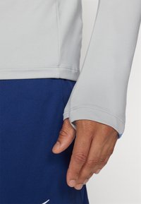 Helles graues Langarmshirt mit einer figurbetonten Passform, das Daumenlöcher an den Bündchen aufweist, kombiniert mit dunkelblauen Shorts. Weicher, elastischer Stoff.
