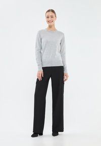 Jasnoszary sweter z długimi rękawami i okrągłym dekoltem, zestawiony z czarnymi spodniami o szerokich nogawkach z bocznymi kieszeniami i gładką teksturą.