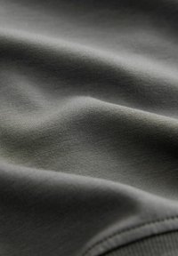 Prim-plan cu un material gri închis, având o textură vizibilă de tricot și pliuri moi care creează umbre delicate.