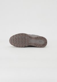 Semelle de chaussure de sport noire avec surface texturée, présentant des rainures et un logo en relief. Matériau en caoutchouc durable pour l'adhérence et la traction.
