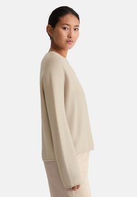 Beige Strickpullover mit lockerer Passform, rundem Halsauschnitt und langen Ärmeln. Der Stoff hat eine strukturierte Oberfläche mit einem subtilen Muster.