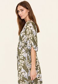 Blumenkleid mit olivgrünem Grund und hellblauen sowie weißen Blattmustern. Mit einem gefältelten Bund und Ärmeln in Dreiviertellänge designt.