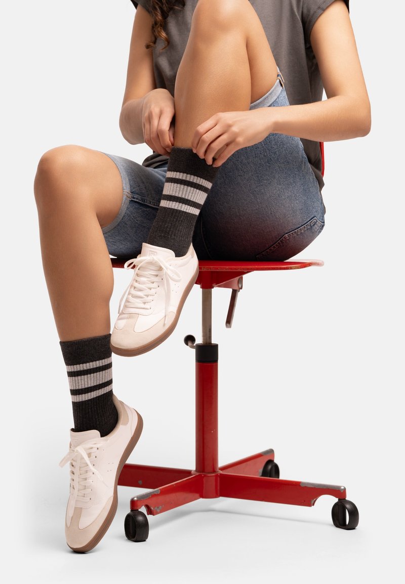 Svarta ribbade strumpor med vita ränder, bärs tillsammans med vita sportskor, denimshorts och sitter på en röd rullstol.