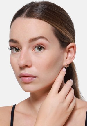 Roze gouden creolen met een knoopontwerp, gedragen aan het oor van een model. Glad textuur, minimalistische uitstraling en subtiele glans.