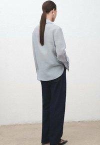 Camisa de manga larga gris claro con cuello, combinada con pantalones de pierna ancha oscuros y zapatos de punta negros. Tela suave con un corte relajado.