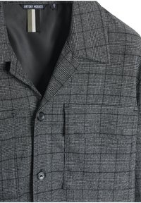 Blazer grigio a quadri con rever a punta, tasca frontale e chiusura con bottone. Presenta un tessuto testurizzato con un sottile motivo a tartan.
