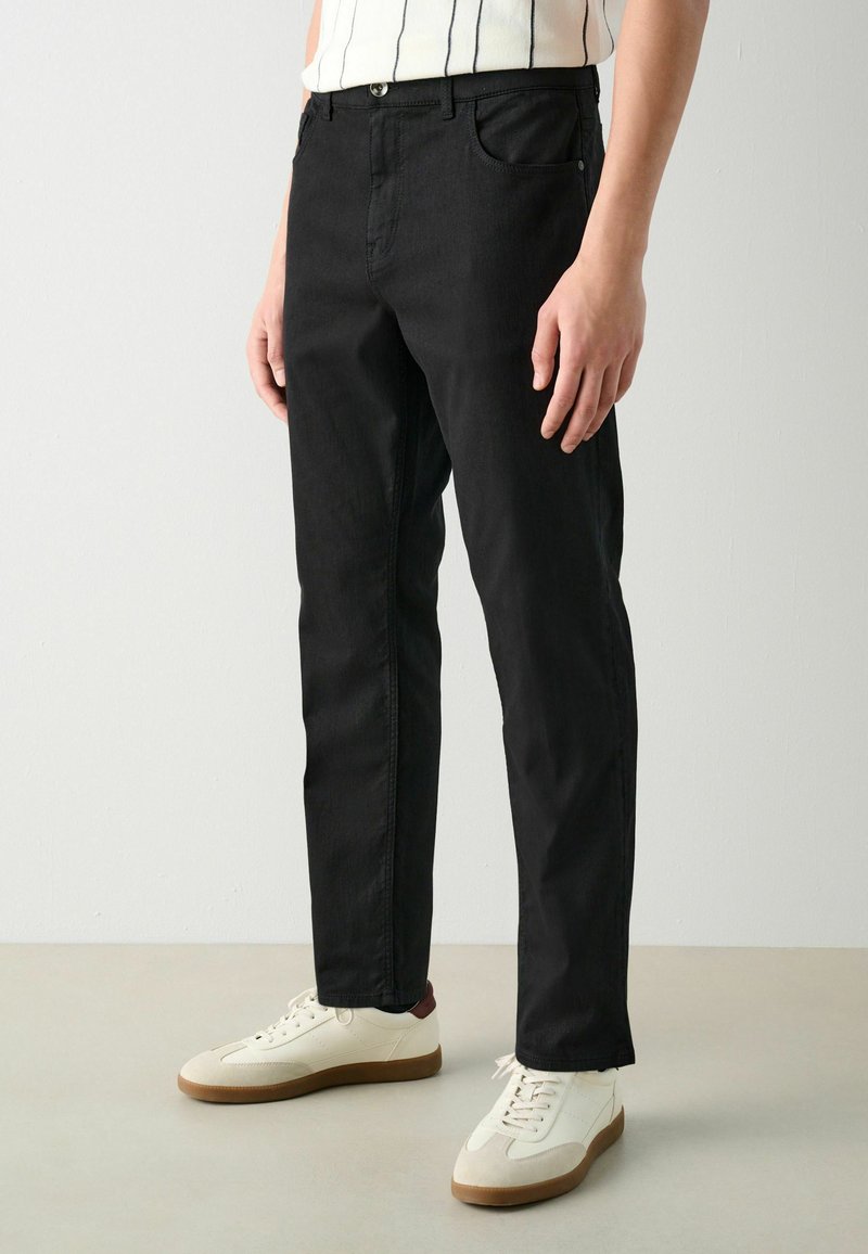 Sorte denimbukser med lige snit, fem lommer og lynlås. Sammen med hvide sneakers med brune detaljer.
