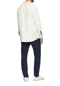 Licht gekleurde langesleeve shirt met een ronde halslijn en marineblauwe accenten, gecombineerd met donkere blauwe broeken en witte sneakers.