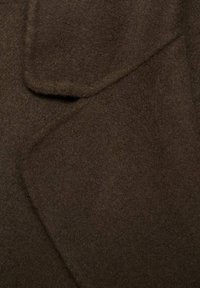 Textil de lana marrón con una textura suave y lisa. Presenta un cuello estructurado y solapas superpuestas, mostrando un tono cálido y rico.