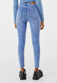 Hoge taille blauwe denim skinny jeans met een vervaagde textuur, twee achterzakken en een onafgewerkte zoom bij de enkel, gecombineerd met zwarte plateau schoenen.