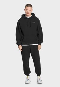 Czarna bluza z kapturem i kieszenią kangurką oraz czarne spodnie dresowe w tym samym kolorze. Charakteryzuje się minimalistycznym wzornictwem i gładką fakturą.