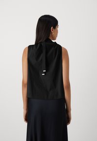 Top nero senza maniche con una texture liscia, dotato di una chiusura posteriore a fiocco e un orlo arrotondato per una vestibilità comoda.