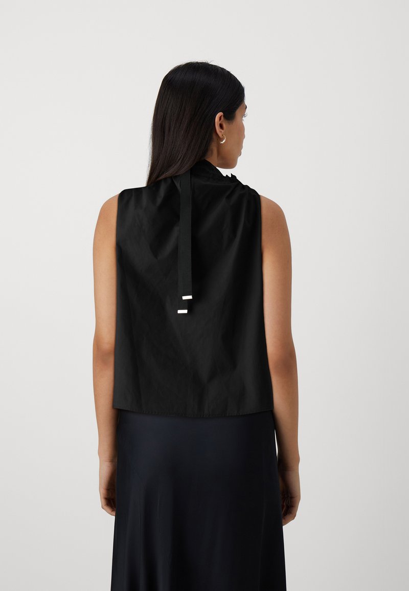 Top nero senza maniche con una texture liscia, dotato di una chiusura posteriore a fiocco e un orlo arrotondato per una vestibilità comoda.