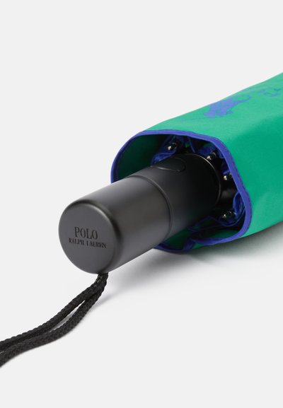 Guarda-chuva dobrável com uma capa de tecido verde e detalhes azuis, apresentando um cabo preto, inscrição de logótipo e uma alça de pulso trançada.