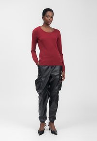 Maglione rosso a maniche lunghe con scollatura rotonda, abbinato a pantaloni cargo in pelle nera con tasche laterali e caviglie risvoltate. Tacchi a punta neri.