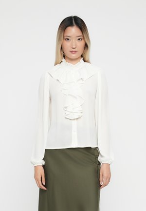 Hvit bluse med volangdesign foran, knappelukking og høy krage. Lange ermer med krøllete mansjetter. Glatt, lett stoff.