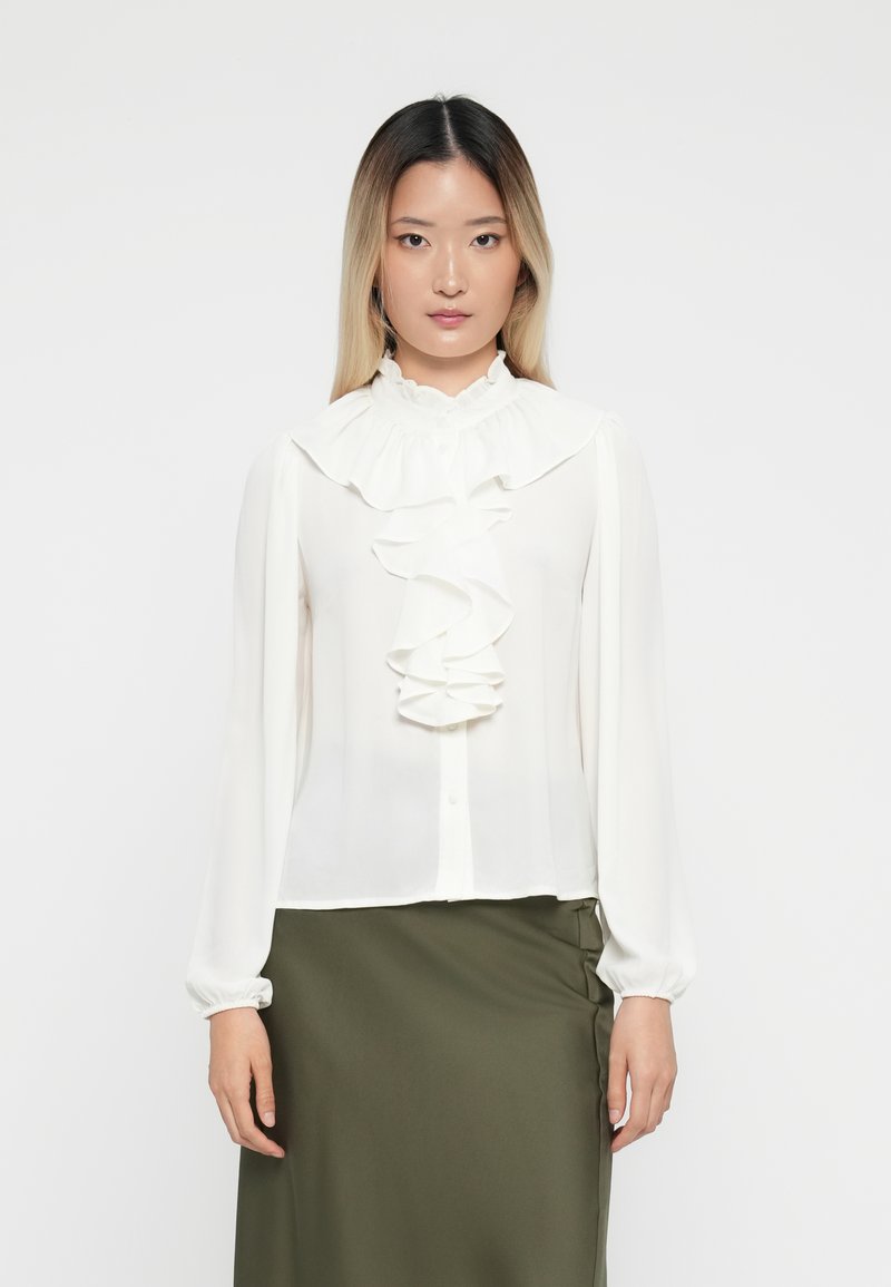 White blouse with ruffled front design, button closure, and high collar. Long sleeves with gathered cuffs. Smooth, lightweight fabric.