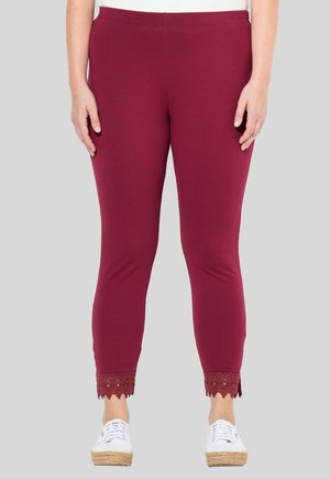 Leggings bordeaux avec une texture lisse et une taille élastique. Présente une bordure en dentelle au bas, accompagnés de baskets blanches.