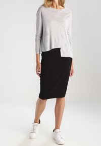 Šedý dlouhý rukáv s kulatým výstřihem, vrstvený přes černou upnutou sukně ke kolenům, doplněný bílými teniskami. Hladká textura.