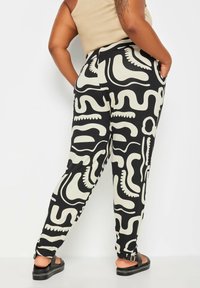 Zwarte broek met een crèmekleurig abstract patroon, met een relaxte pasvorm, zijzakken en een gladde stoftextuur. Verhoogd met een elastische tailleband.