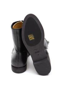 Black leather ankle boots with a smooth finish, rounded toe, low heel, and interior lining in tan. Sole features embossed brand detail.