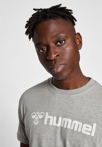 Grijze katoenen T-shirt met korte mouwen, voorzien van een opvallend wit "hummel" logo. Glad textuur en ronde hals.