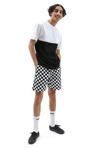 Zwart-witte kleurgeblokte t-shirt met korte mouwen, gecombineerd met zwart-witte geruite shorts. Zwarte sneakers en witte sokken.