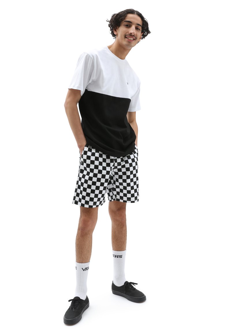 Zwart-witte kleurgeblokte t-shirt met korte mouwen, gecombineerd met zwart-witte geruite shorts. Zwarte sneakers en witte sokken.