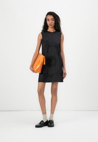 Black sleeveless dress with a floral pattern, paired with an orange leather clutch, worn with beige socks and black loafers.
