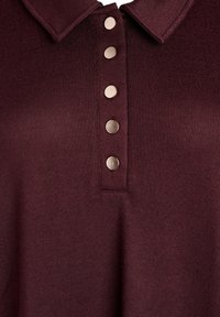 Burgunderrotes Strickoberteil mit kurzem Kragen und fünf Metallknöpfen vorne. Strukturierter Stoff mit figurbetonter Form.