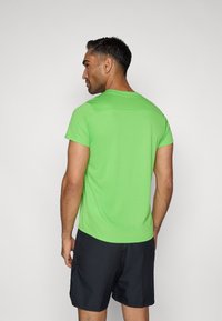 Πράσινο αθλητικό μπλουζάκι με κοντά μανίκια, φτιαγμένο από απαλό ύφασμα, με στρογγυλή λαιμόκοψη και ελαφρώς καμπυλωτό στρίφωμα. Φορεμένο με μαύρη βερμούδα.