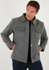 Jachetă gri din lână cu guler, două buzunare pe piept și buzunare laterale, cu închidere cu capse și finisaj texturat.