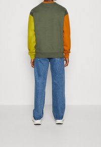 Felpa con blocchi di colore in pannelli verdi, gialli e arancioni; vestibilità morbida; rifinita con polsini e orlo a coste, abbinata a jeans larghi blu.