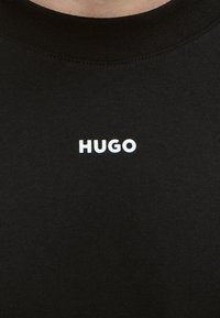 Camiseta negra de cuello redondo con el texto blanco "HUGO" centrado en el pecho.