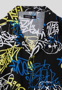 Camicia a maniche corte con uno sfondo nero e motivi in stile graffiti colorati in blu, giallo e bianco; realizzata in tessuto leggero.