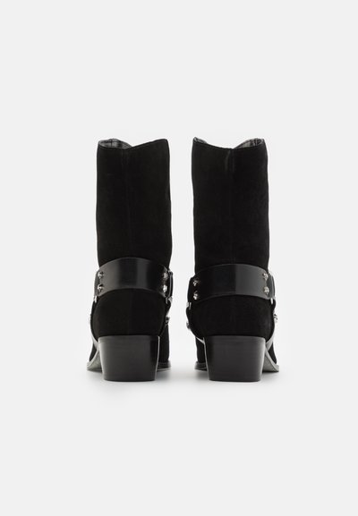 Pair of black suede mid-calf boots with low block heels and decorative black leather straps with silver studs at the back.