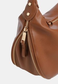 Borsa a mano in pelle marrone con superficie texture, dotata di una cerniera e dettagli in hardware dorati. Forma curva e chiusura a bottone a pressione.