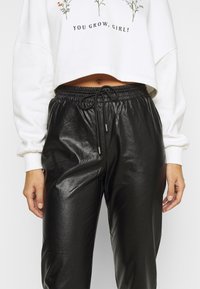 Svarta fusk läderbyxor med en glänsande yta, med elastiskt midjeband och dragsko. Stylat med en kortärmad vit sweatshirt ovanför.