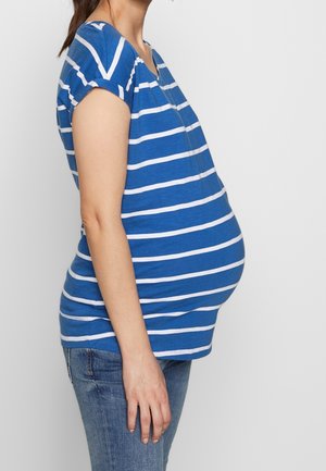 Niebieska pasiasta bluzka ciążowa z miękkiego materiału, krótki rękaw, luźny krój, z zaokrąglonym dołem, noszona z jasnoniebieskimi dżinsami.