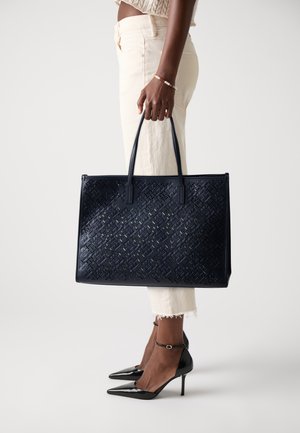 Sac fourre-tout bleu foncé en matériau texturé, présentant un motif tissé, deux poignées et une forme structurée.