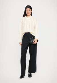 Pull en crème texturé avec un col en V et une coupe loose, associé à un pantalon large taille haute noir et un petit sac à main noir. Accompagné de bottines noires.