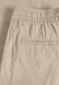 Beige Shorts mit elastischem Bund und geraffter Textur sowie einer Gesäßtasche mit rechteckiger Öffnung, aus leichtem Stoff gefertigt.