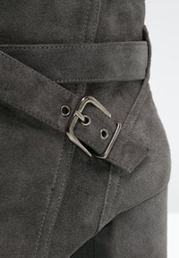 Grauer Wildlederstiefel mit silberner Metallschnalle und Riemendetails, die die Nahaufnahme der Textur und der Nähte im oberen Teil des Schuhs zeigt.