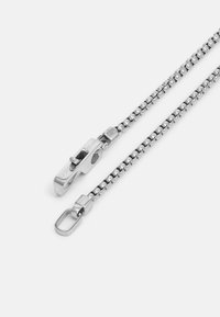 Chromen metalen ketting met een slank ontwerp, voorzien van een unieke sluiting en een ovale schakel. De gladde textuur en glanzende afwerking versterken de uitstraling.
