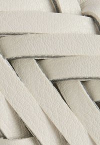 Strisce di pelle intrecciata di colore bianco morbido, con una superficie texturizzata e bordi scuri a contrasto, creando un motivo a strati.