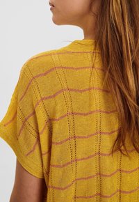 Gul stickad topp med horisontella rosa ränder, lös passform, korta ärmar och en texturerad design med öppna stygn detaljer.