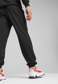 Sorte joggers med ribbet talje og ankler, parret med hvide og røde atletiksko med et særpræget design og teksturerede mesh-paneler.