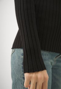 Černý žebrovaný top s dlouhým rukávem a přiléhavým střihem, s jemnou texturou, kombinovaný se světle modrými džíny s mírným zesvětlením.