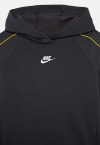 Juodas gobtuvas su kengūros kišene, geltonais akcento siūlais ir balta Nike logotipu ant krūtinės. Pagamintas iš minkštos, lengvos medžiagos.